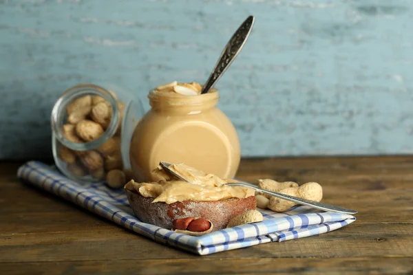 Sanduíche saboroso e frasco com manteiga de amendoim fresco no fundo de madeira — Fotografia de Stock