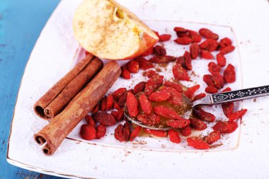 Olgun elma, tatlım kaşık, goji meyveleri ve tarçın beyaz kare plaka üzerinde mavi ahşap arka plan