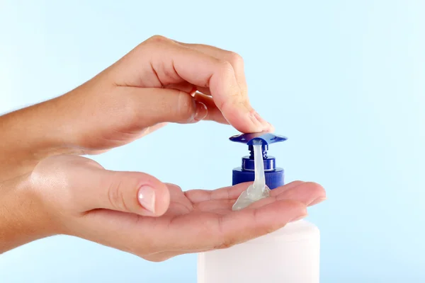 Manos femeninas usando jabón líquido sobre fondo azul claro — Foto de Stock