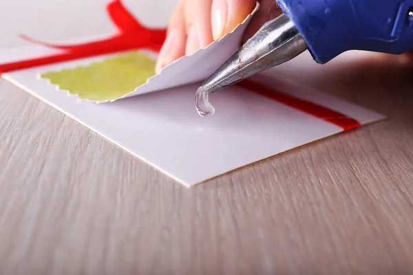 Vrouw hand maken ansichtkaart met rood lint en boog met behulp van lijmpistool — Stockfoto