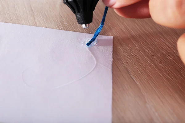 Woman's hand making postcard with blue ribbon with a help of glue gun — Stock Photo, Image