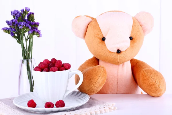 Toy bear and cup of raspberries on napkin on wooden wall background — Stock Photo, Image