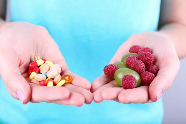 Woman holding berries and pills on grey background — Stock Photo, Image