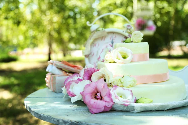 Bolo de casamento bonito com flores na mesa, ao ar livre — Fotografia de Stock