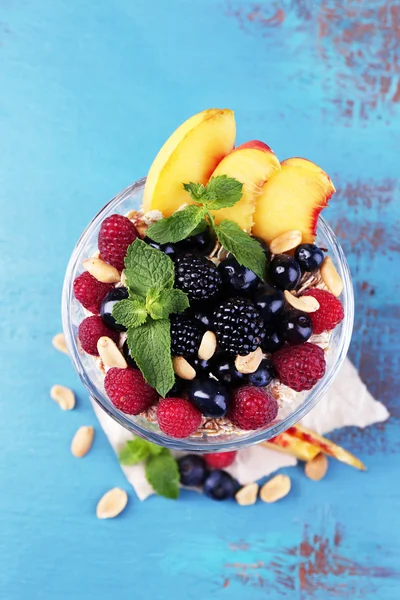 Colazione sana - yogurt con frutta fresca, bacche e muesli serviti in una ciotola di vetro su sfondo di legno a colori — Foto Stock