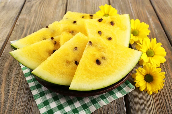 Slices of yellow watermelon on checkered napkin and yellow flowers on wooden background — Stock Photo, Image