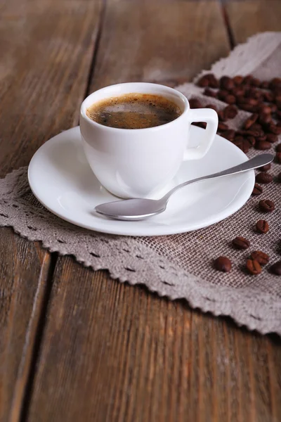 Cup of coffee with milk and coffee beans on napkin on wooden background — Stock Photo, Image