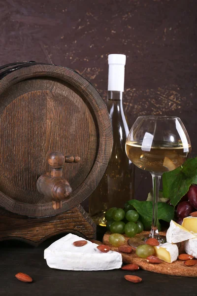 Cena compuesta de queso Camembert, vino y uvas sobre tabla de cortar y barril de vino sobre mesa de madera sobre fondo marrón — Foto de Stock