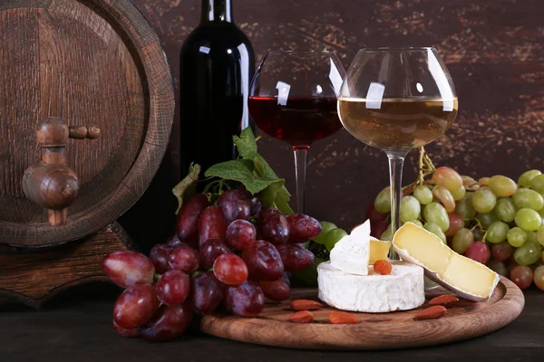 Supper consisting of Camembert cheese, wine and grapes on cutting board and wine barrel on wooden table on brown background — Stock Photo, Image