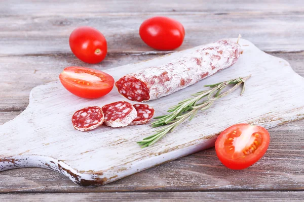 Salami français aux tomates sur planche à découper sur fond bois — Photo