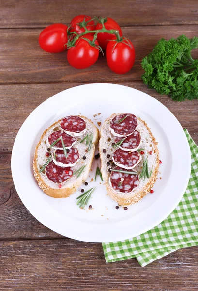 Sandwiches with salami on plate on napkin on wooden background — Stock Photo, Image