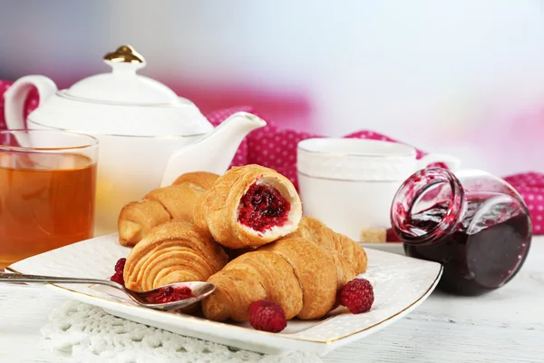 Frukost med te, äppeljuice, sylt och färska croissanter på träbord, på ljus bakgrund — Stockfoto
