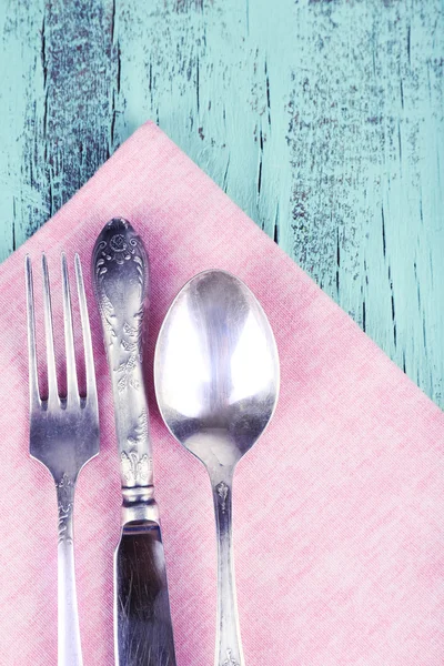 Naczynia stołowe, owinięte w liliowy serwetka na niebieskim tle drewniane — Zdjęcie stockowe