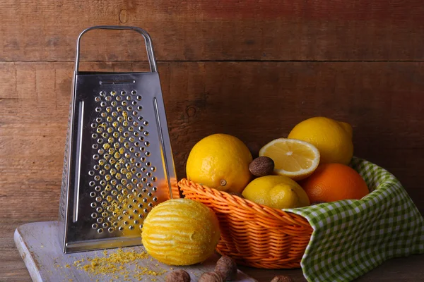 Lemons on napkin in basket, cutting board and grater on wooden background — Stock Photo, Image