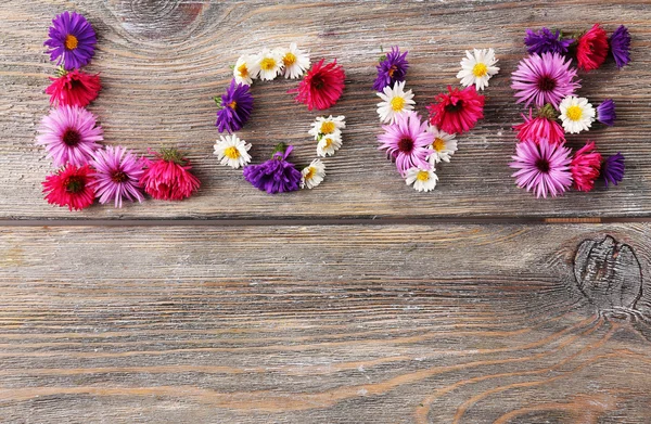 Liebeswort geformt mit kleinen Blumen auf Holzgrund — Stockfoto