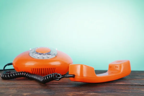 Старый красный телефон на деревянном столе на синем фоне — стоковое фото