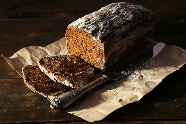 Plátky žitného chleba a nůž na papír řemesla na prkénko na dřevěné pozadí — Stock fotografie