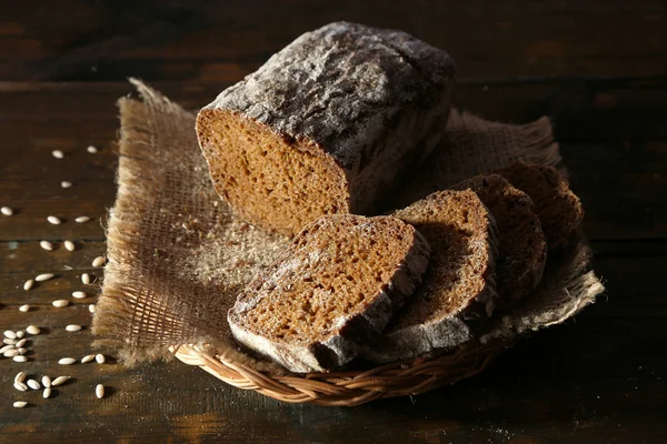 Sliced rye bread on sackcloth napkin on wicker basket on wooden background — Stock Photo, Image