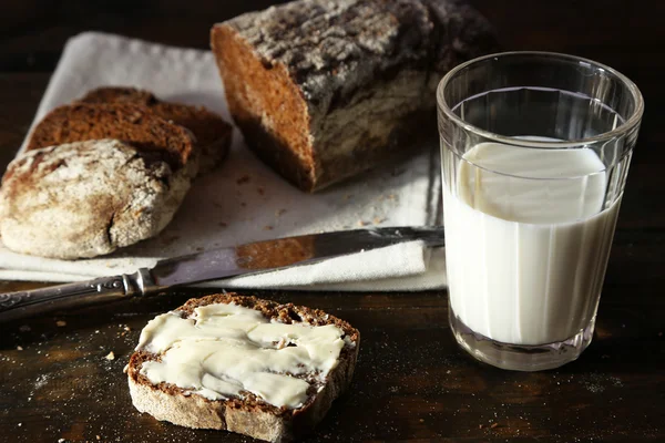 Roti gandum diiris, segelas susu segar dan pisau di serbet putih dengan latar belakang kayu — Stok Foto