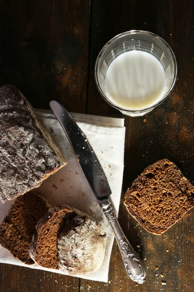 Roti gandum diiris, segelas susu segar dan pisau di serbet putih dengan latar belakang kayu — Stok Foto