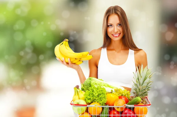 Concetto di shopping. Bella giovane donna con frutta e verdura nel carrello della spesa su sfondo negozio — Foto Stock