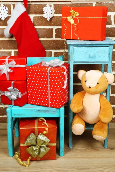 Рождественские подарки на стуле и книжный шкаф на фоне коричневой кирпичной стены — стоковое фото