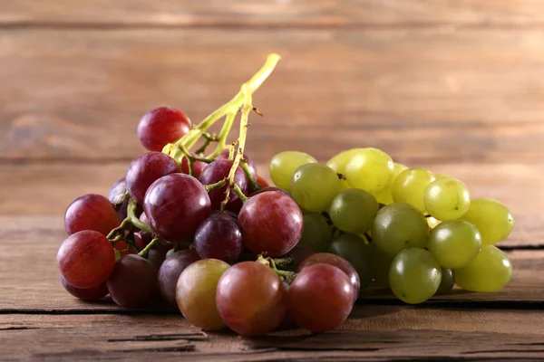 Trauben verschiedener Arten von Trauben auf Holztisch vor Holzwandhintergrund — Stockfoto