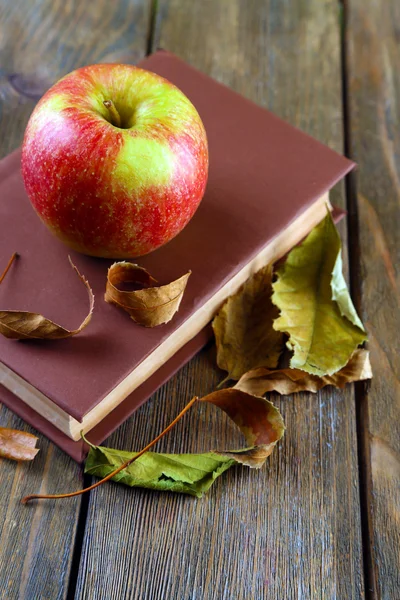 Manzana con libro y hojas secas sobre fondo de madera — Foto de Stock