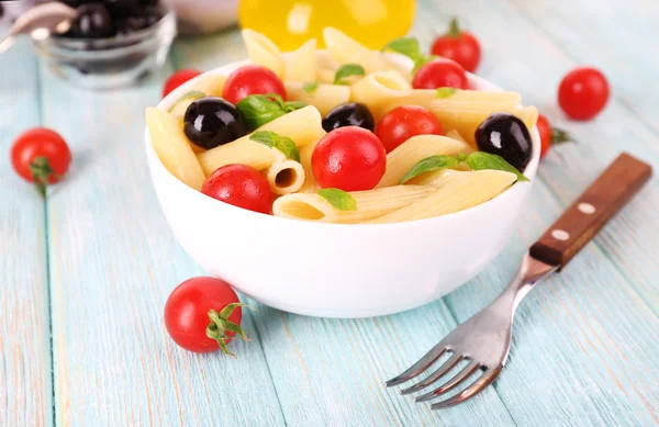 Nudeln mit Tomaten, Oliven und Basilikumblättern in Schüssel und Serviette auf Holzgrund — Stockfoto