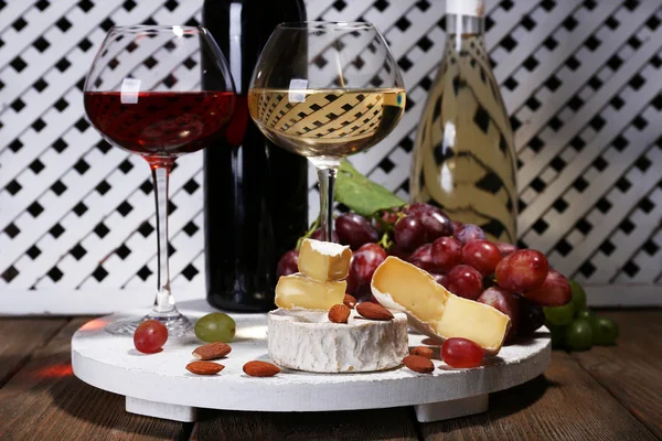 Cena compuesta por queso Camembert, vino y uvas en pie sobre mesa de madera sobre fondo de valla blanca — Foto de Stock