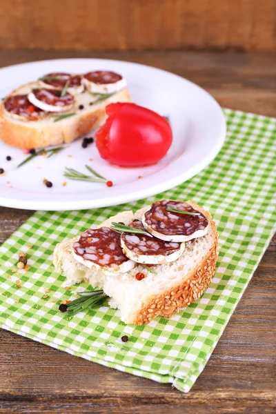 Sandwiches with salami on plate and on napkin on wooden background — Stock Photo, Image