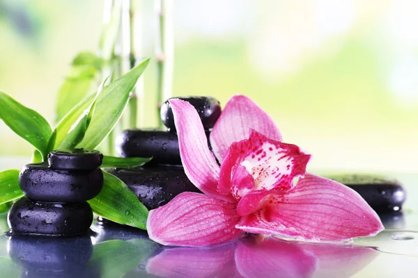 Piedras de spa, ramas de bambú y orquídea lila en la mesa sobre fondo natural —  Fotos de Stock