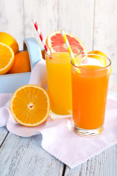 Jus d'orange et de carotte dans des verres sur serviette et fruits frais dans une boîte en bois sur table en bois sur fond mural en bois — Photo