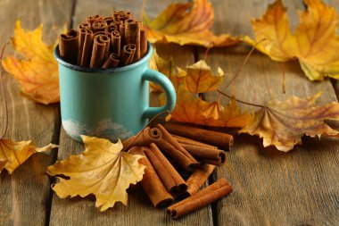 Ahşap zemin üzerine sarı yaprakları ile bardağa tarçın sopa