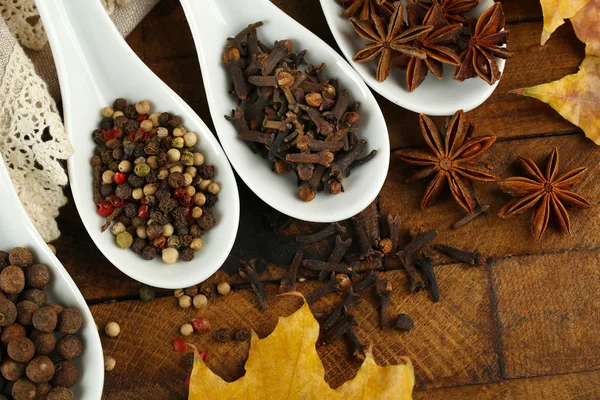 Different spices in spoons with yellow leaves on wooden background — Stock Photo, Image