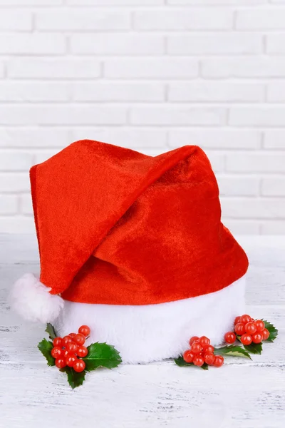 レンガ壁の背景にテーブルの上のクリスマス帽子とヤドリギの葉 — ストック写真