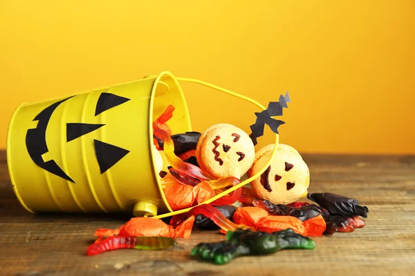 Doces diferentes para festa de Halloween na mesa de madeira, no fundo amarelo — Fotografia de Stock