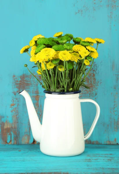 Yellow and green flowers in decorative teapot on color wooden background — Stock Photo, Image