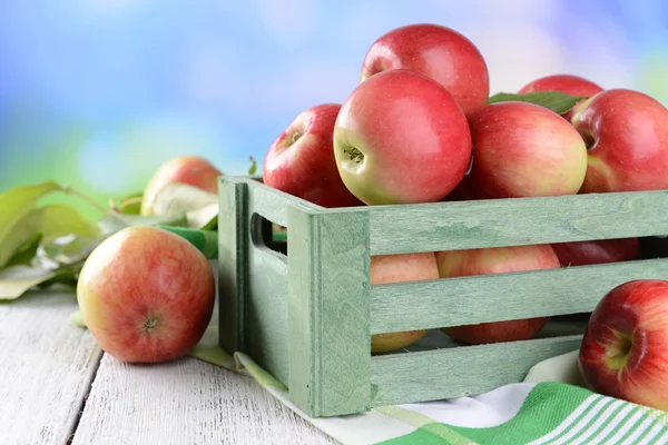 Сладкие яблоки в деревянной коробке на столе на ярком фоне — стоковое фото