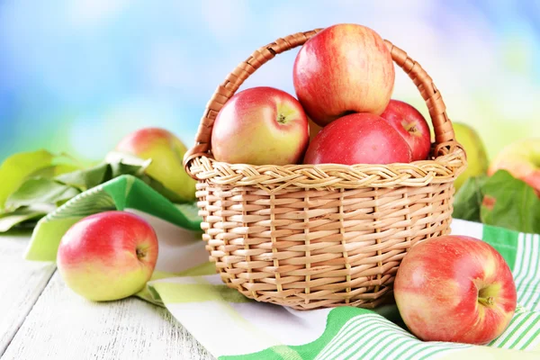 Manzanas dulces en canasta de mimbre sobre mesa sobre fondo brillante — Foto de Stock