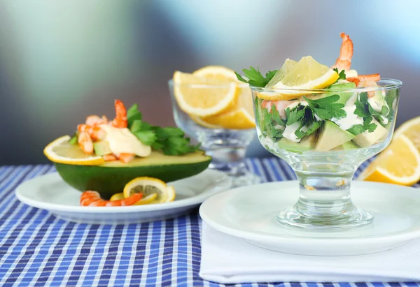 Tasty salads with shrimps and avocado in glass bowl and on plate, on table, on bright background — Stock Photo, Image