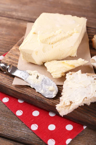 Fresh homemade butter on paper and sliced bread, on cutting board, on wooden background — Stock Photo, Image