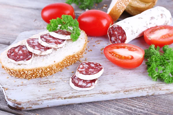 French salami with tomatoes, parsley and bread on cutting board on wooden background — Stock Photo, Image