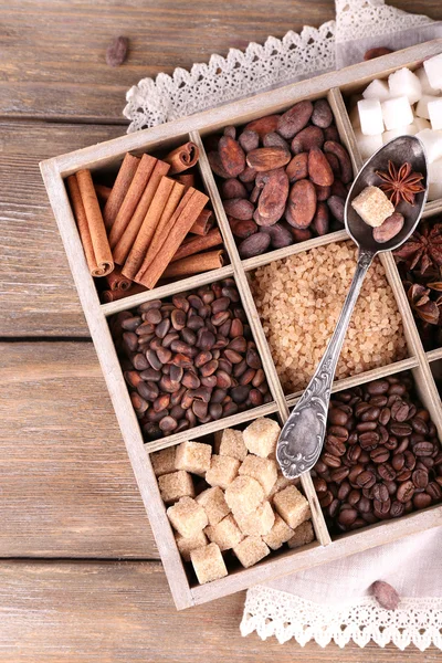 Wooden box with set of coffee and cocoa beans, sugar cubes, dark chocolate, cinnamon and anise, close-up, on wooden background — Stock Photo, Image