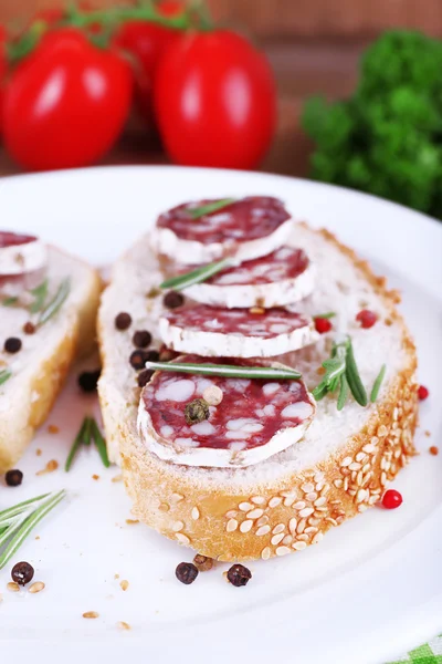 Sandwiches with salami on plate on napkin on wooden background — Stock Photo, Image