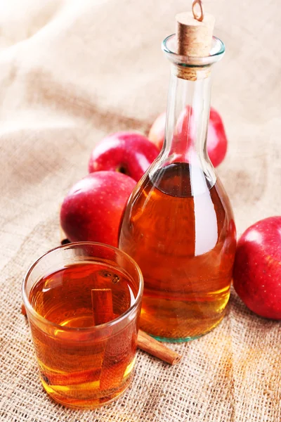 Apple cider med kanelstänger och färska äpplen på säckväv bakgrund — Stockfoto
