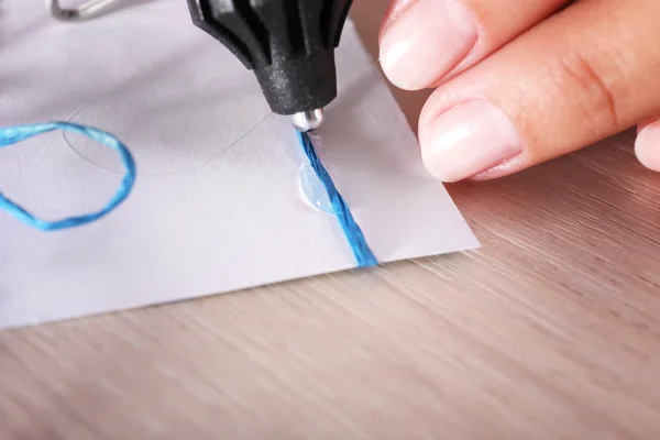 Woman's hand making postcard with blue ribbon and bow with a help of glue gun — Stock Photo, Image