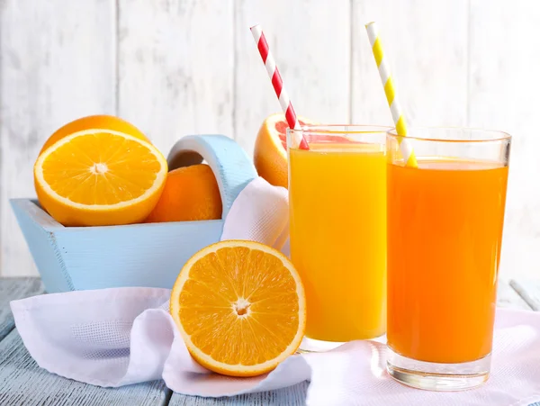 Oransje og gulrotsaft i glass på serviett og frisk frukt i trekasse på trebord på veggens bakgrunn – stockfoto