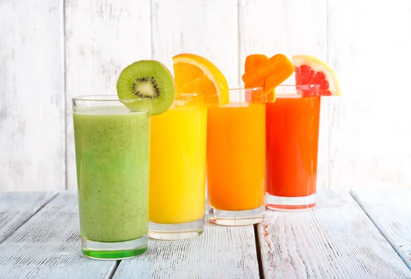 Suco de frutas e vegetais em copos e pedaços de frutas frescas na mesa de madeira no fundo da parede de madeira — Fotografia de Stock