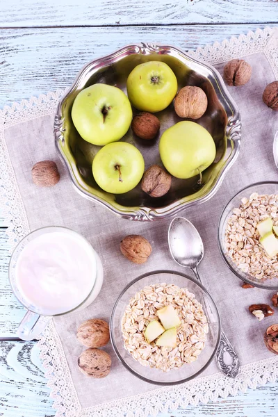 Harina de avena en cuencos, nueces, manzanas y yogur sobre servilleta sobre fondo de madera azul — Foto de Stock